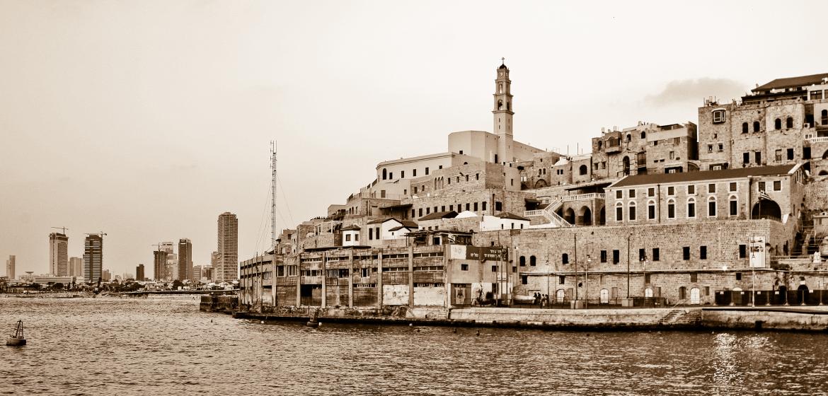 Der alte Hafen von Jaffa und die Skyline Tel Avivs. Die Protagonisten Ariel und Alaa wohnen beide im gleichen Haus in Tel Aviv. Als Ariel nach Alaa’s Verschwinden dessen Notizbuch findet, stößt er dabei auch auf Alaas Erinnerungen an seine Großmutter, an deren Erfahrung der Nakba und an ein historisches Jaffa, das heute nicht mehr existiert. Foto: Wikimedia.