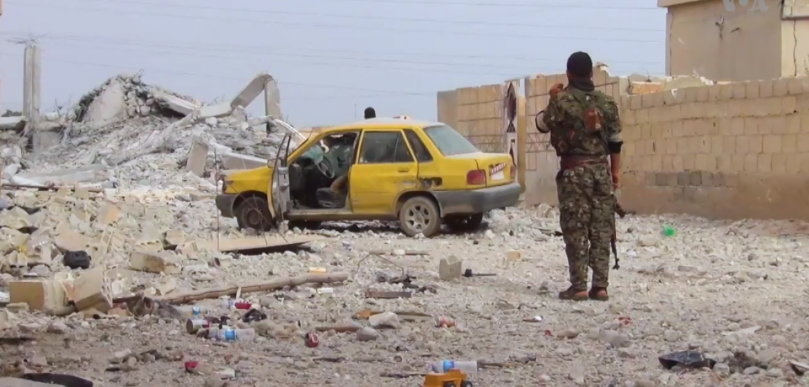 Ein Kämpfer der "Syrian Democratic Forces" (SDF) steht Anfang Mai nach tagelangen Kämpfen gegen Da'esh in der zerstörten Stadt Taqba in Nord-Syrien. Foto: Mahmoud Bali (VOA), Wikicommons, Public Domain. https://commons.wikimedia.org/wiki/File:SDF_in_Tabqa_1.png