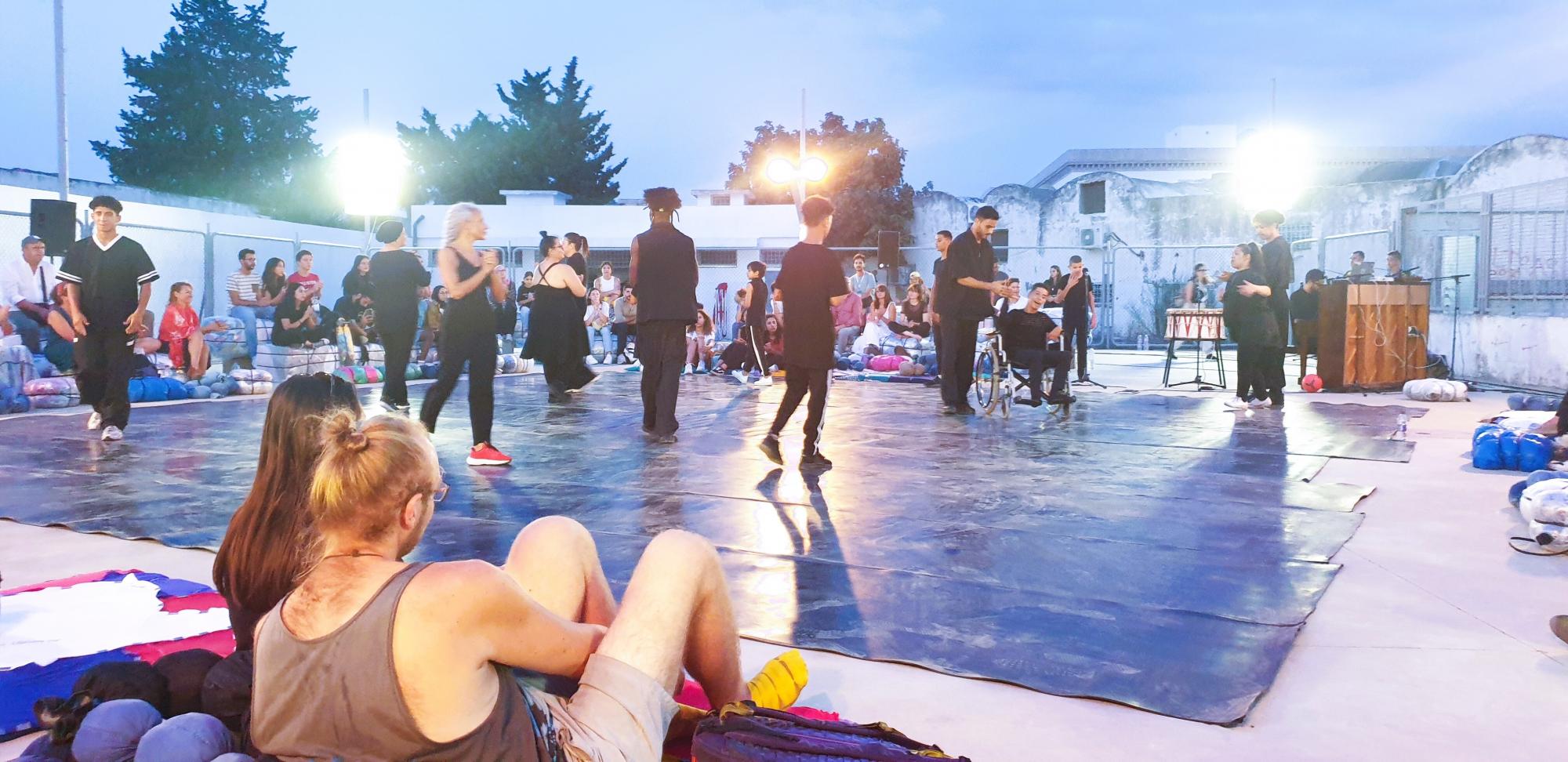 An der inklusiven Performance „Lines“ sind viele Tänzer:innen und Musiker:innen - sowohl Profis als auch Laien mit und ohne Behinderung -  beteiligt und beschäftigen sich mit dem Zusammenleben in der Stadt. Ringsum die Bühne sitzen die Zuschauenden. Foto: Vanessa Barisch.