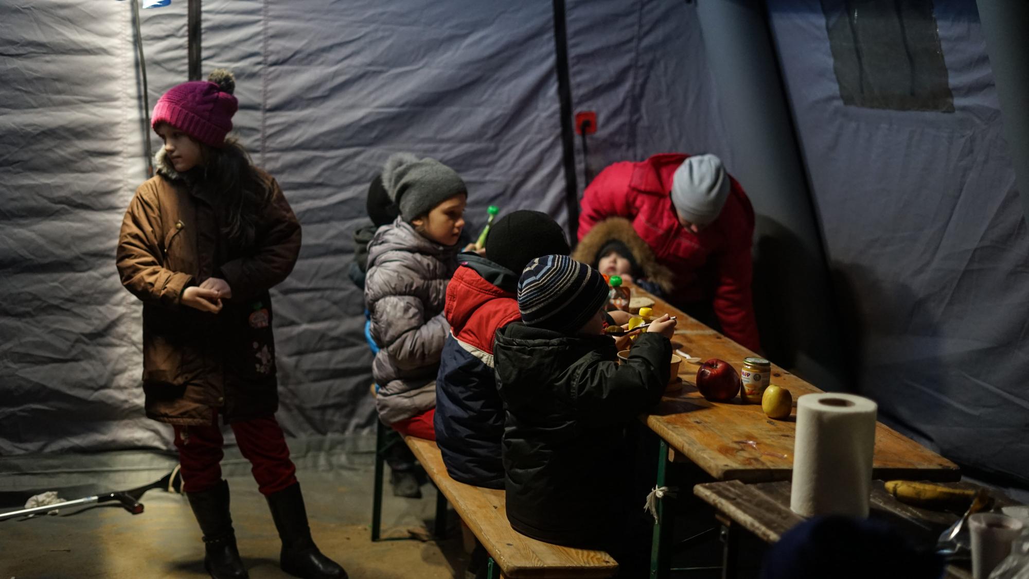 Ukrainische Kinder warten in einem Zelt an der Grenze zwischen Polen und der Ukraine, wo einige Organisationen und Freiwillige Hilfsmittel zur Verfügung stellen. Budomierz, 05.03.2022. Foto: Milad Amin