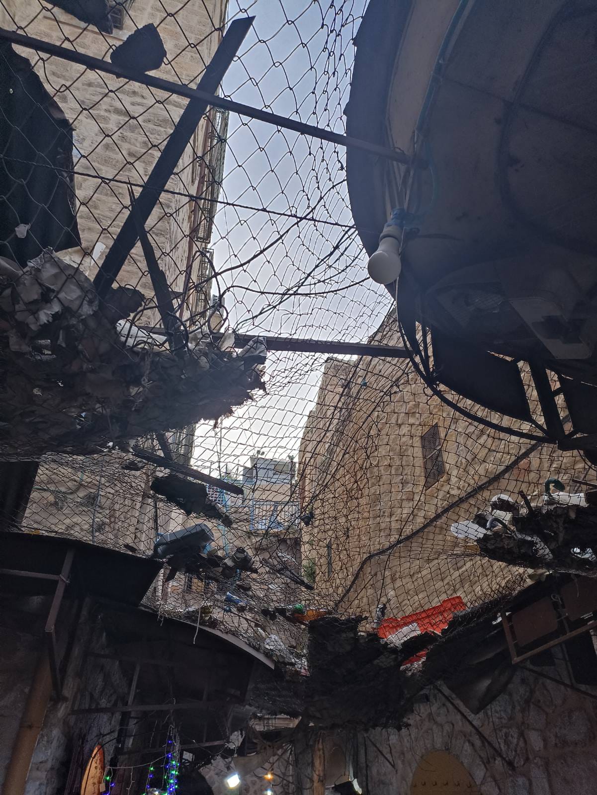 Eine israelische Siedlung direkt über einer Marktstraße in der Altstadt von Hebron. Palästinenser:innen mussten Gitter aufstellen, um sich vor dem Müll zu schützen, den die Siedler:innen auf sie werfen. Foto: Izzat Karaki